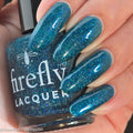 Blue glittery nail polish with 'firefly lacquer' branding held by a hand.