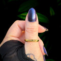Hand with purple nail polish wearing a gold ring against a dark background