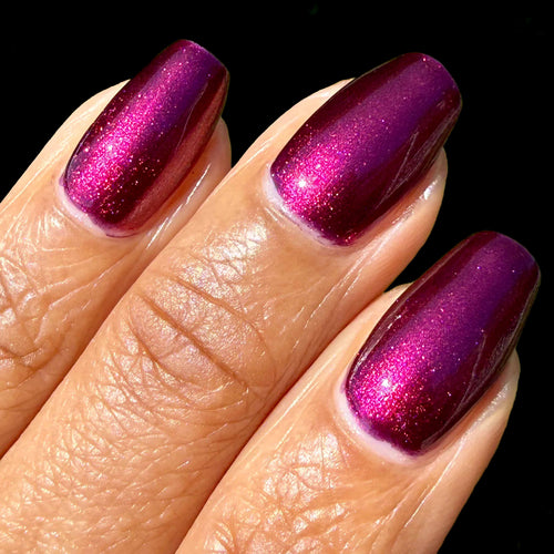 Close-up of three fingernails painted with a glossy metallic magenta-purple nail polish showing fine shimmer, against a black background.