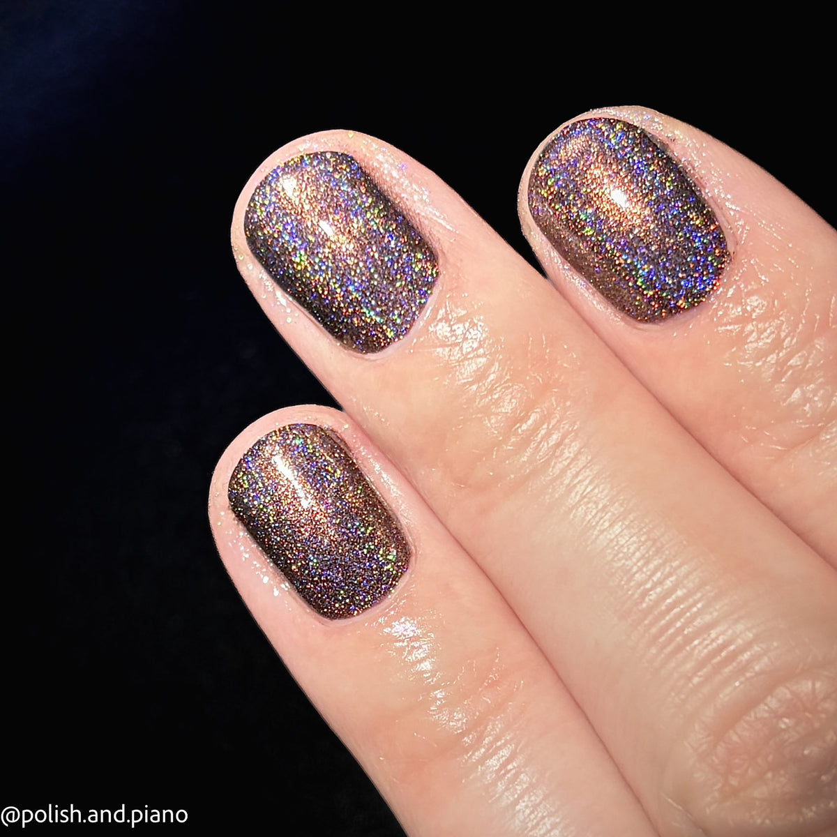 Close-up of a hand with fingernails painted in a dense, shimmery holographic glitter polish that shifts between bronze, gold, and purple against a black background.