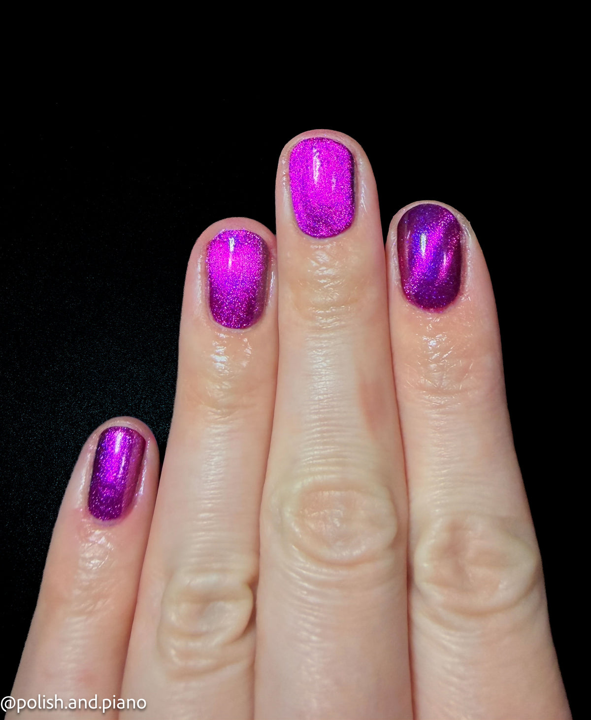 A close-up of a hand with fingernails painted in a sparkling metallic magenta-purple polish against a solid black background.