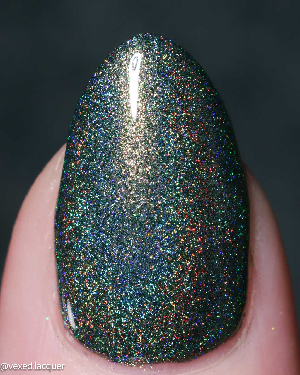 A close-up of a fingernail painted with a dark, highly reflective glitter polish that shifts between black, green, and iridescent rainbow tones.