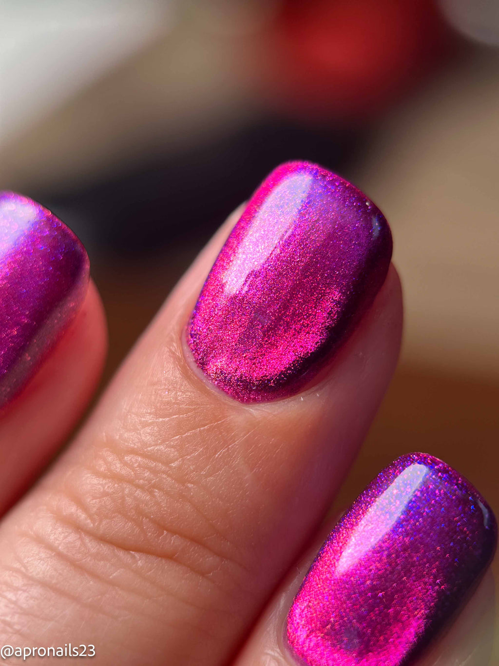 Close-up of fingernails painted with a vivid iridescent magenta and purple nail polish, showing a shimmering color shift under light.