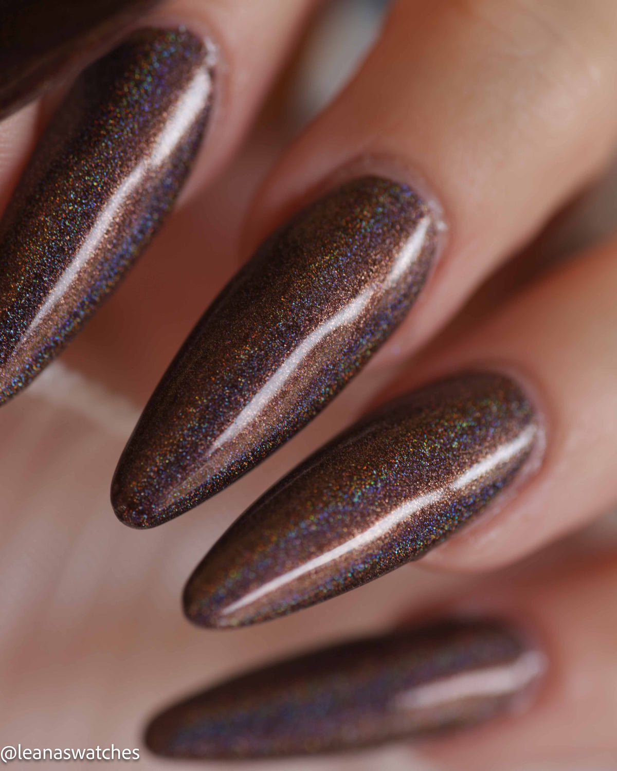 Close-up of a hand with long almond-shaped nails painted in a dark brown holographic nail polish that shifts with iridescent glitter.