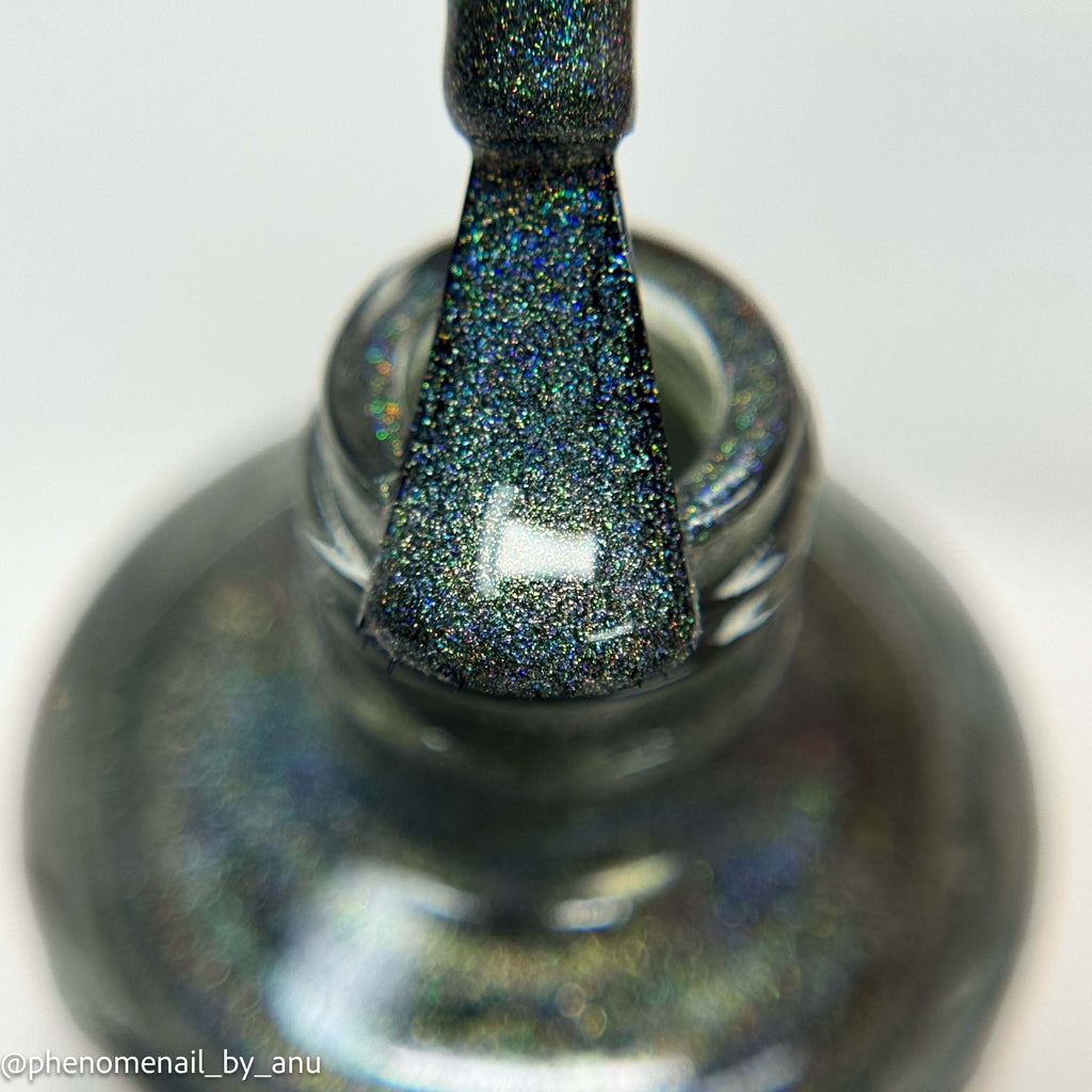 Close-up of a glittery dark gray nail polish brush resting in a matching bottle, showing a shimmering iridescent finish on a white background.