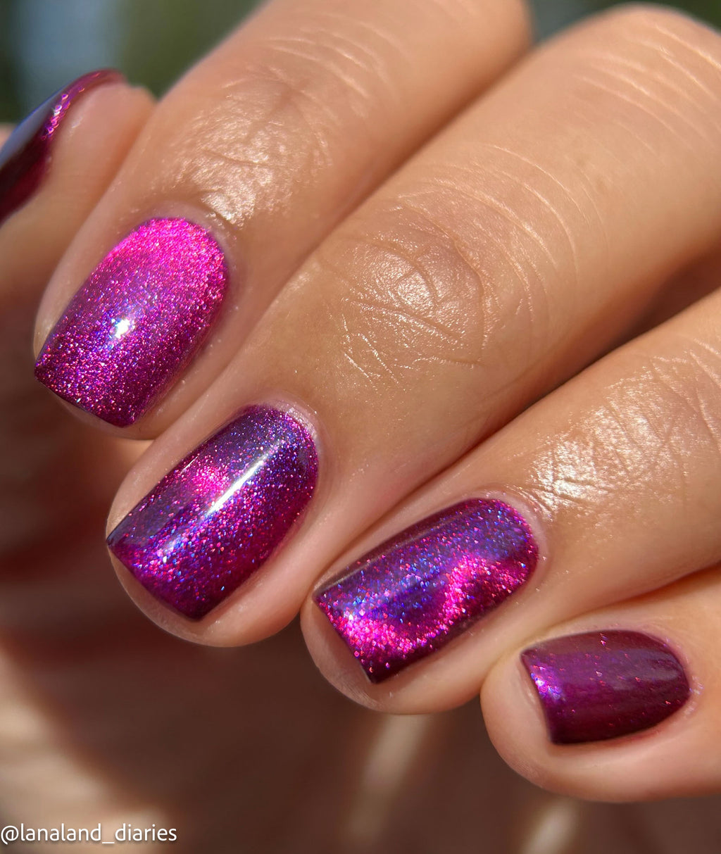 Close-up of a hand with manicured nails painted in a sparkling magenta and purple holographic glitter polish.