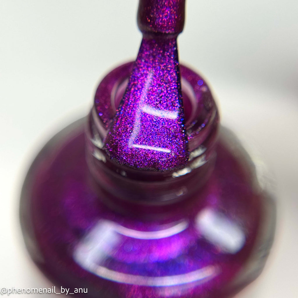Close-up of a purple glitter nail polish bottle with the brush applying polish to a nail, showing a sparkling magenta-purple finish against a soft white background.