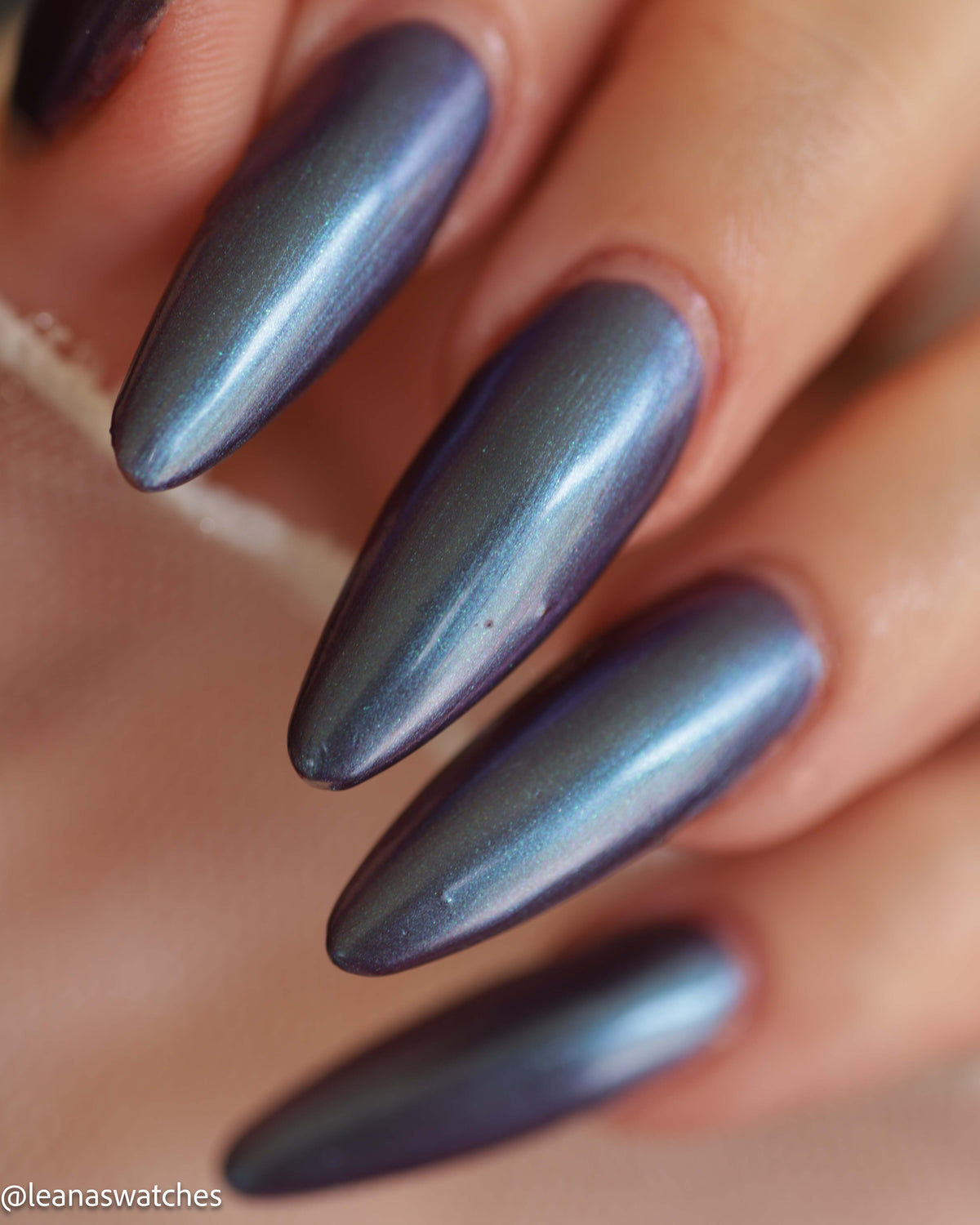 Close-up of a hand with long almond-shaped nails painted in a shimmery metallic blue-gray nail polish.