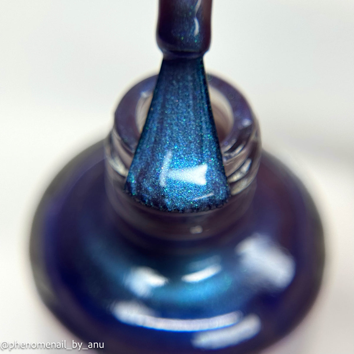 Close-up of a blue metallic nail polish brush stroke applied to a glass bottle, showing a shimmering deep blue color with fine glitter.
